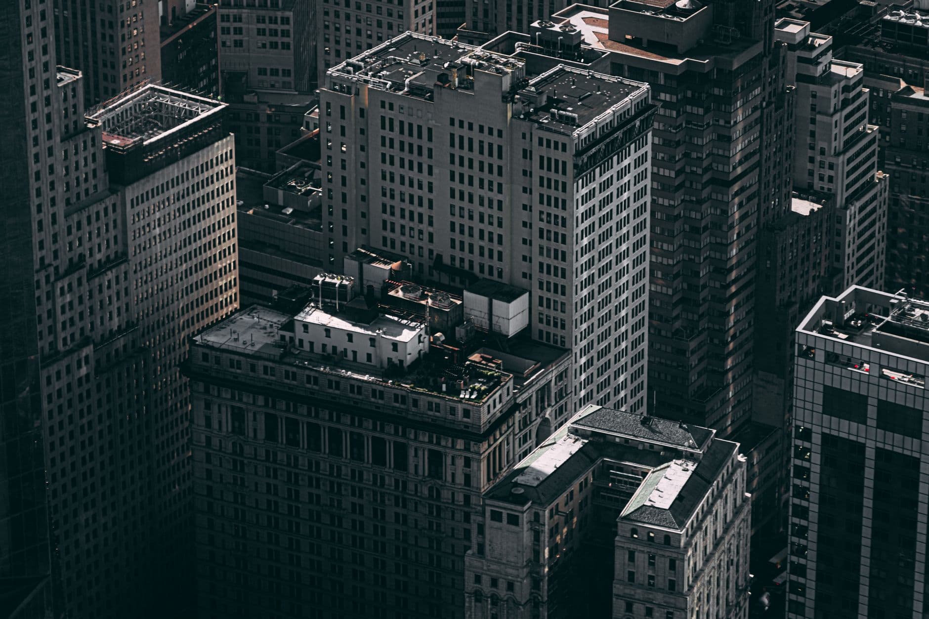 Elevated view over a dense cluster of Manhattan office buildings, their rooftops and window grids rendered in muted gray tones.