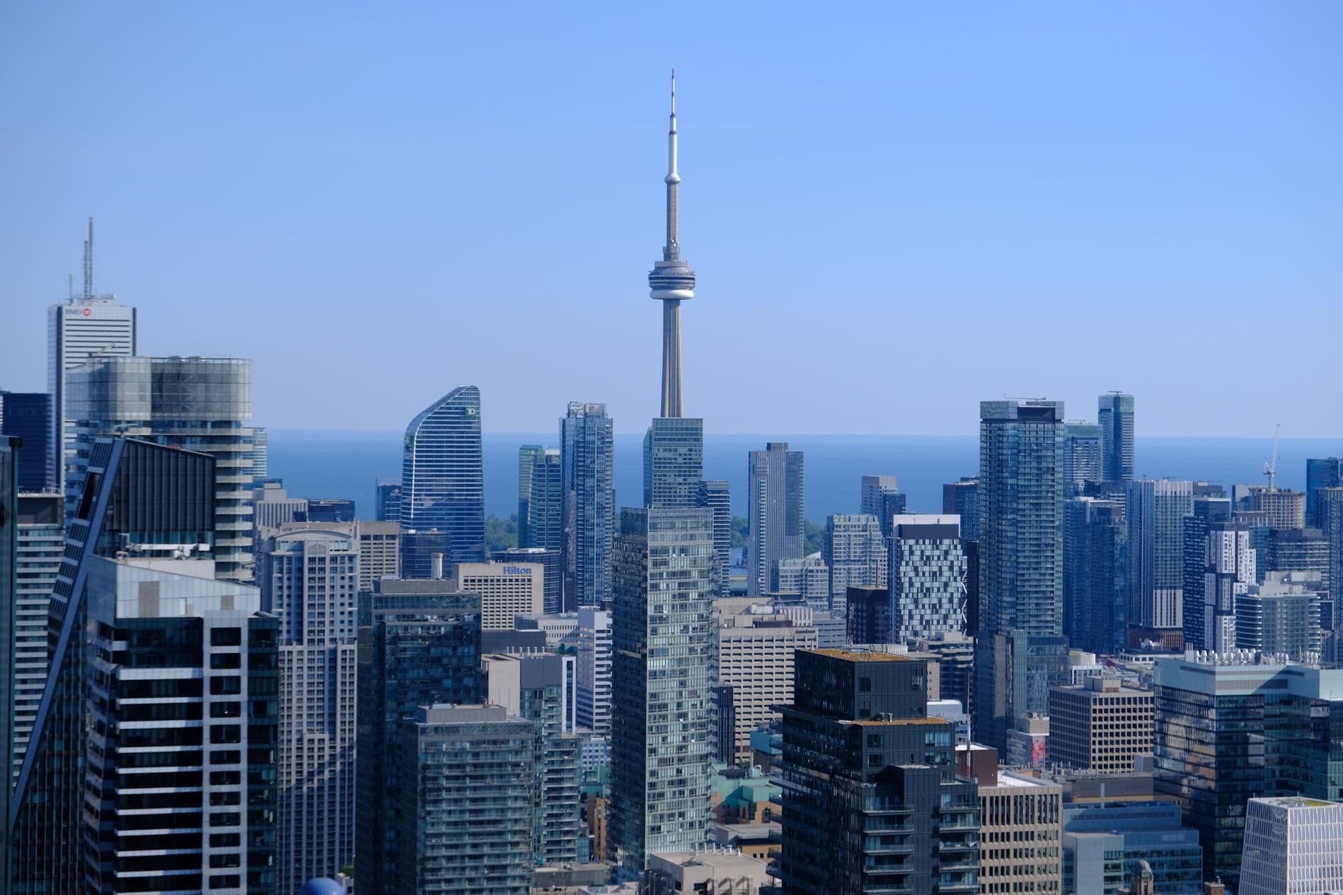 Elevated daytime view of downtown Toronto office towers with the CN Tower and Lake Ontario in the distance.