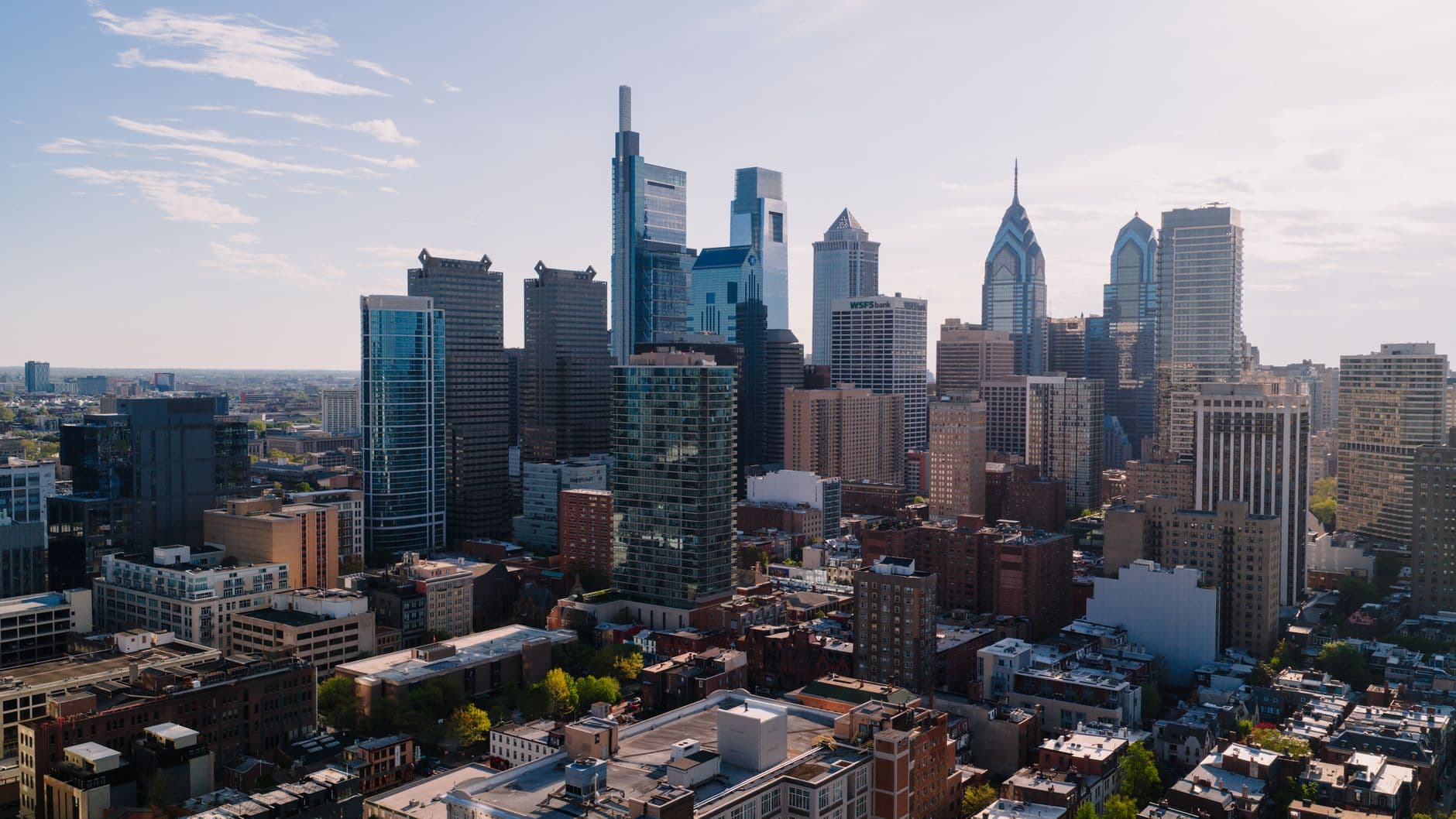 Aerial view of Center City Philadelphia's office towers and surrounding rowhouse blocks in daylight.