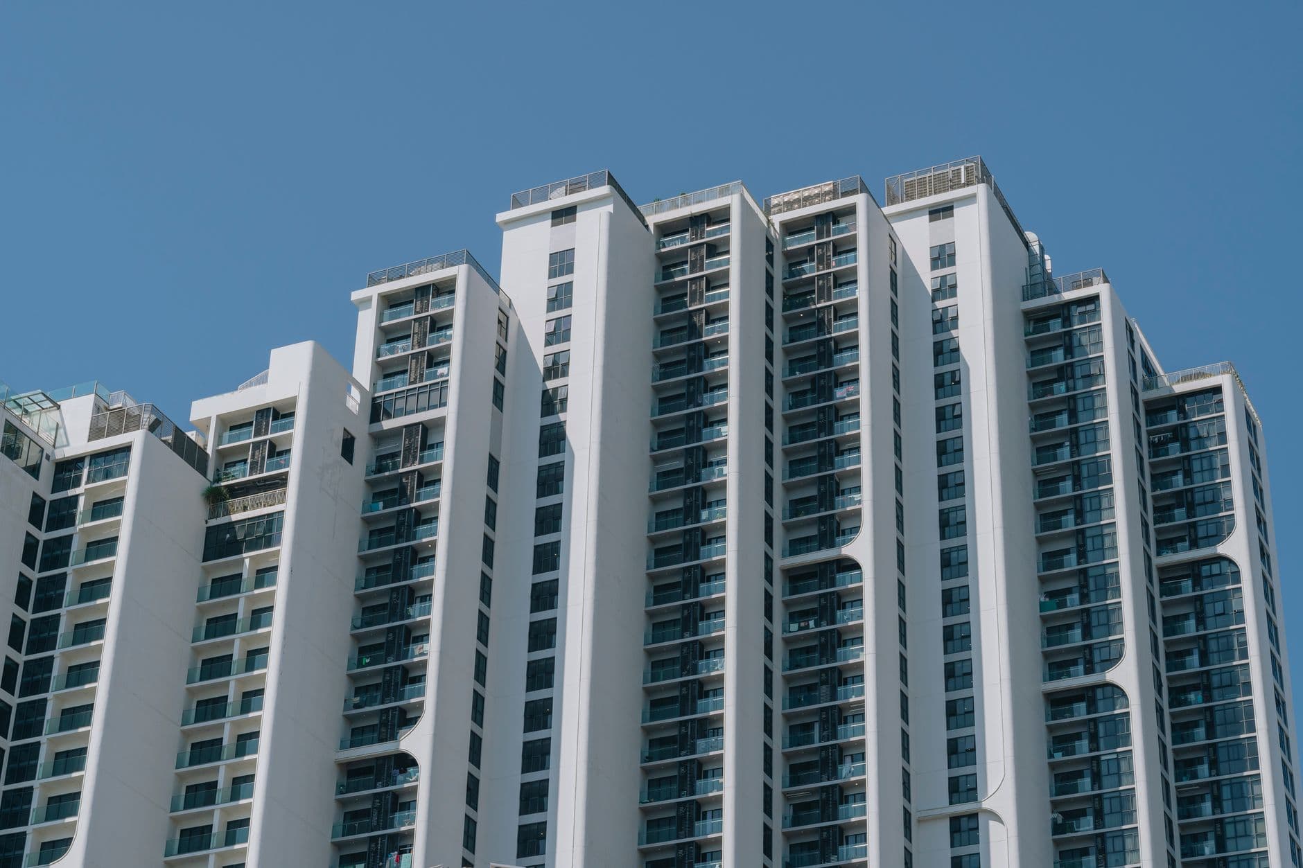 Upper floors of a white multi-tower apartment complex photographed from below against a clear sky.