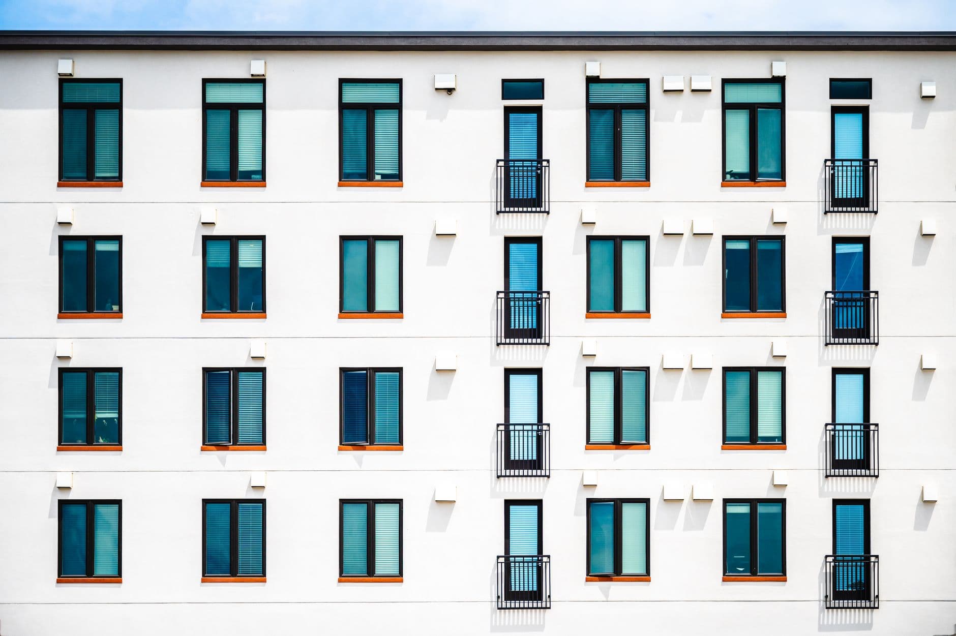 Frontal view of a white mid-rise apartment building with an even grid of windows and small railed balconies.