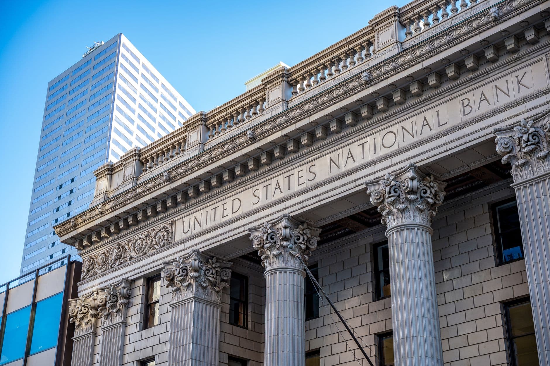 Corinthian columns and carved stone entablature of the United States National Bank building, with a modern office tower rising behind.