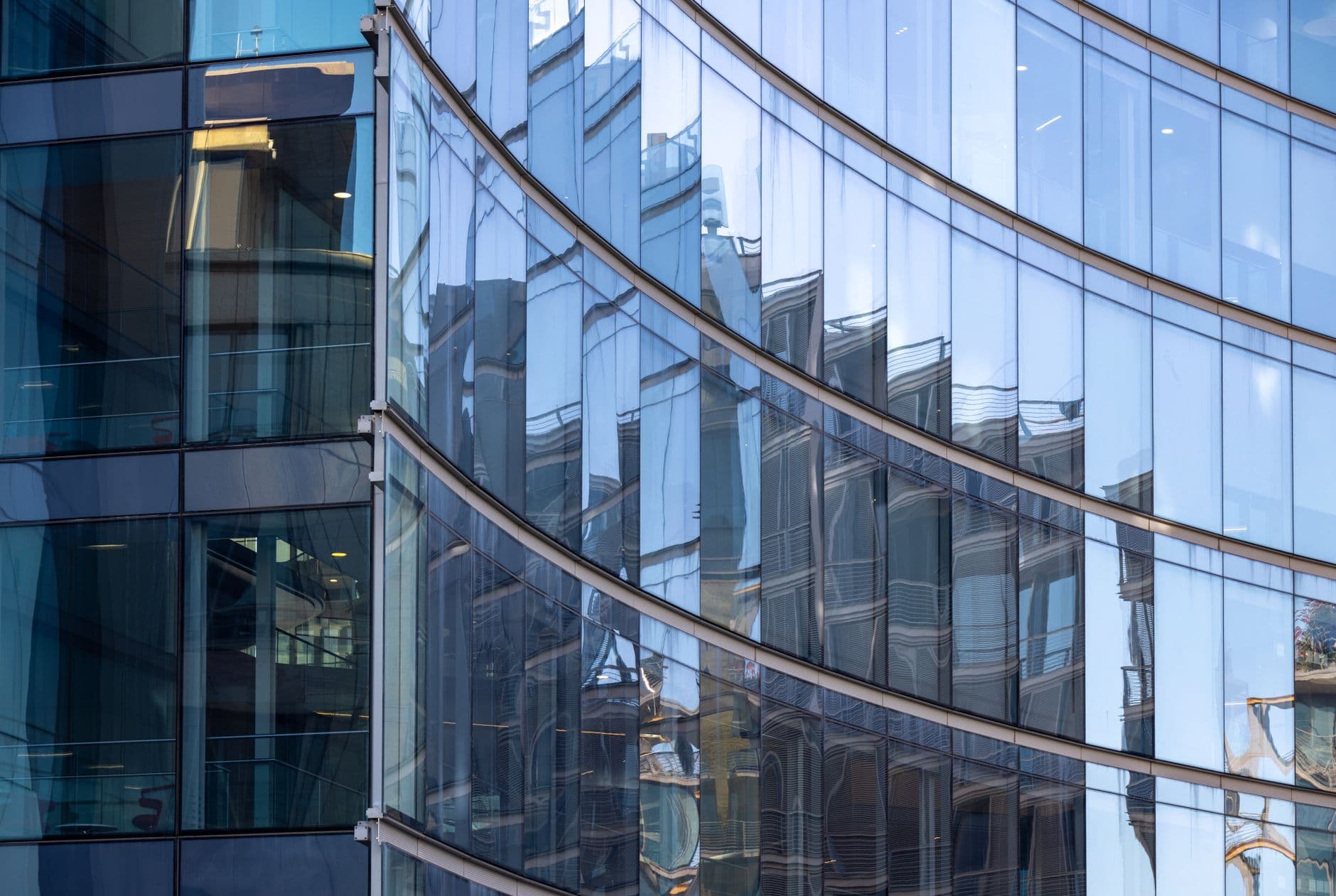 Curved curtain-wall glass facade reflecting the distorted outlines of neighboring buildings.
